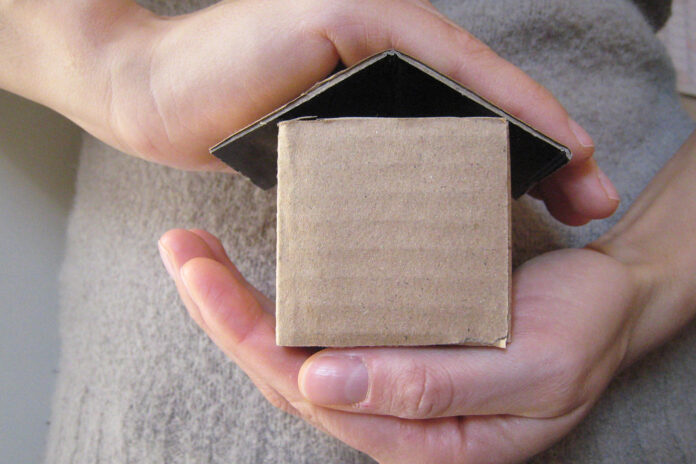 Due mani che proteggono una casa di cartone