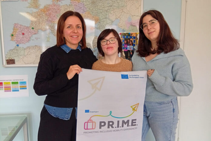 Una ragazza disabile insieme a due educatrici che sostengono un cartellone del progetto