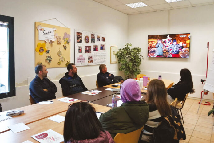 Varie persone sedute ad un tavolo che guardano la tv in un ufficio